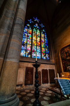 Prague, Czechia - 05 October 2026: View of the vibrant stained glass window inside St. Vitus Cathedral, featuring intricate stone walls and a tall candle stand in the foreground.