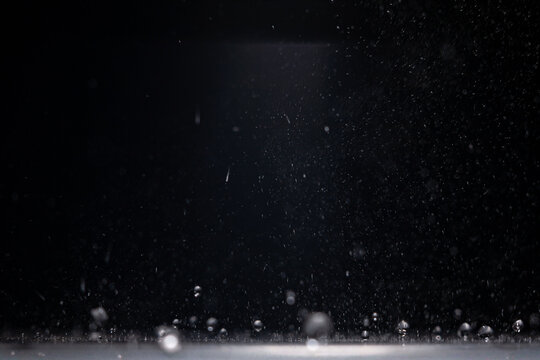 Water droplets falling through a dark space and landing on a lit surface