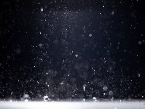 Water droplets falling through a dark space and landing on a lit surface