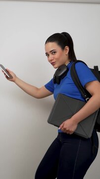 Young latina female college student with backpack and headphones dancing and using her smartphone