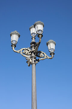 Ornate multi-light street lamp in Spain, against a clear blue sky in a minimalist composition