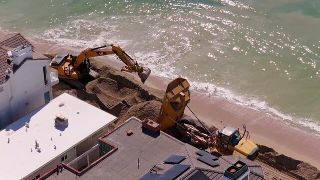 Long Beach, California, USA - October 15, 2026: Excavator spreads sand unloaded by a dump truck, shaping the berm as waves wash ashore below homes on the Peninsula after Tropical Storm Rachel.
