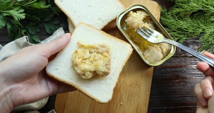 Woman making sandwich with cod liver at wooden table, top view