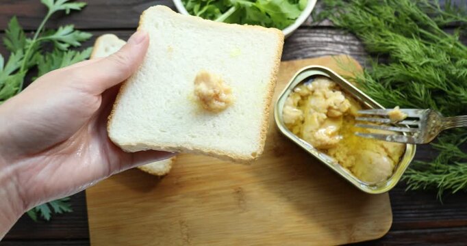 Woman making sandwich with cod liver at wooden table, top view