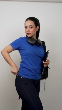 Beautiful latina young female student holding a laptop and wearing headphones, putting her phone in his jeans pocket, isolated on a white background