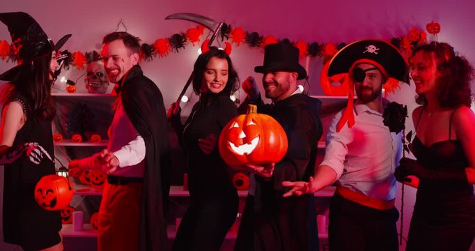 Happy Halloween friends, holiday people dancing wearing costumes for dress ups party night event, playing spooky horror cosplay look, garland red light decor atmosphere, pumpkin lantern decor at home