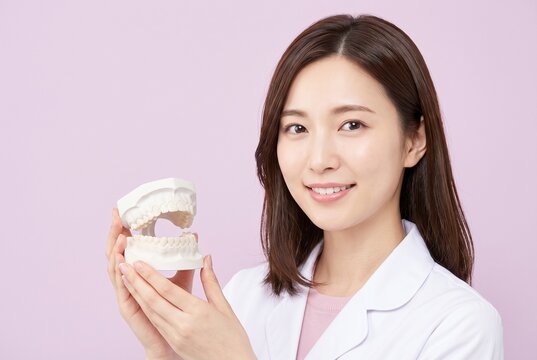 淡いピンク背景で歯科治療を説明する女性ドクター、歯科医院の広告向け