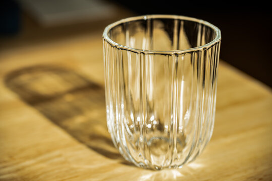 A ribbed glass catches the golden afternoon sunlight, casting an intricate, elongated shadow across a warmly illuminated wooden table surface, Victoria, Australia