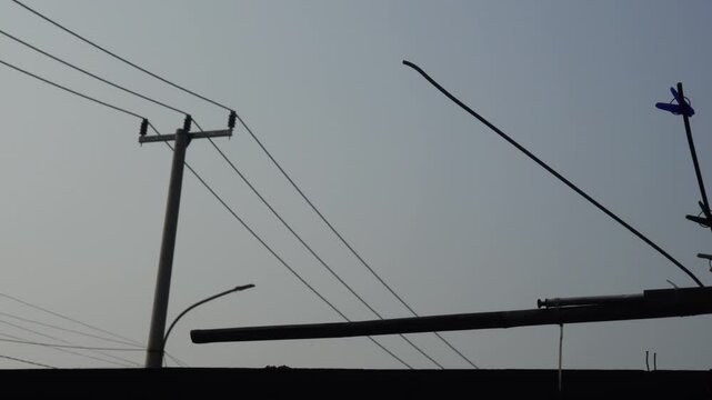 Silhouette of utility power lines and poles against a clear pale sky background.