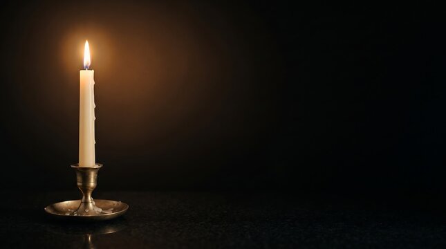 Single lit ivory taper candle in antique brass holder with dripping wax on black granite, quiet Christmas night