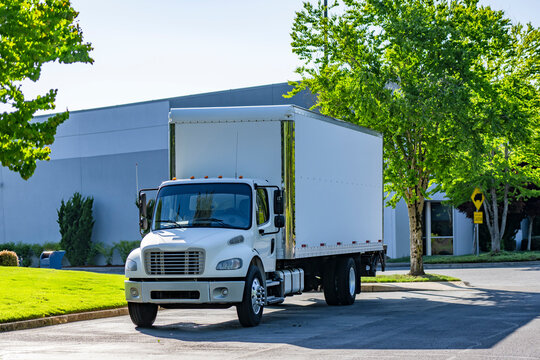 Clean white middle duty rig semi trick with day cab and box trailer standing on the industrial parking lot at sunny day waiting for the next local deliveries