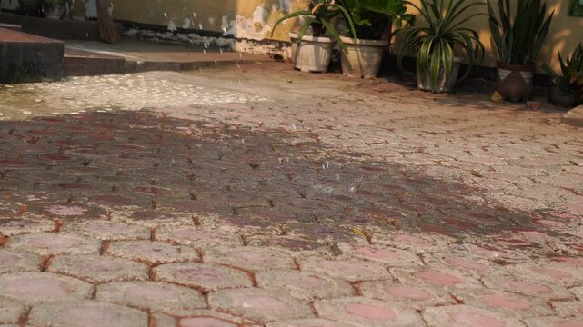 Static ground level shot of water splashing onto dry hexagonal yard paving blocks.