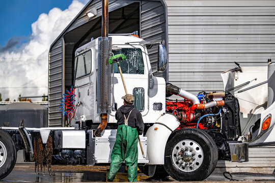Day cab white big rig semi truck with open hood standing at the car wash place with washer working on it
