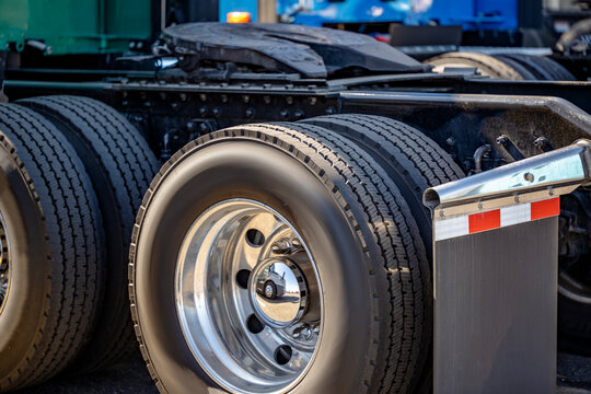 Green Big rig semi truck tractor with new tires on the rims of dual wheels and paired drive axles standing on the truck stop parking lot in row with another semi trucks