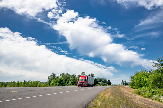 Red big rig semi truck with pipe grille guard transporting cargo in dry van semi trailer driving on the flat highway road