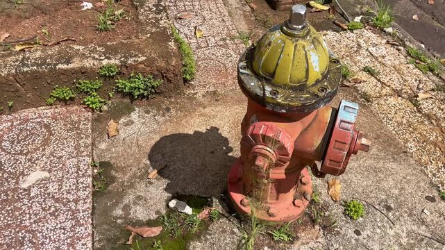 A classic outdoor fire hydrant installed on a concrete sidewalk background. A high-angle close-up view showcasing a weathered red metal fireplug with a yellow top cap casting a distinct shadow 