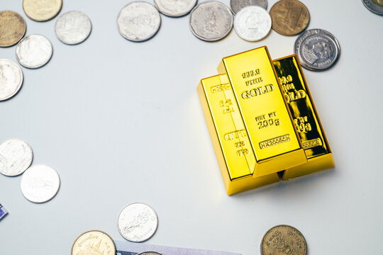High angle view of stacked gold bars surrounded by scattered coins on a white background, representing gold investment, wealth, saving, financial security and a safe haven asset in times of inflation.