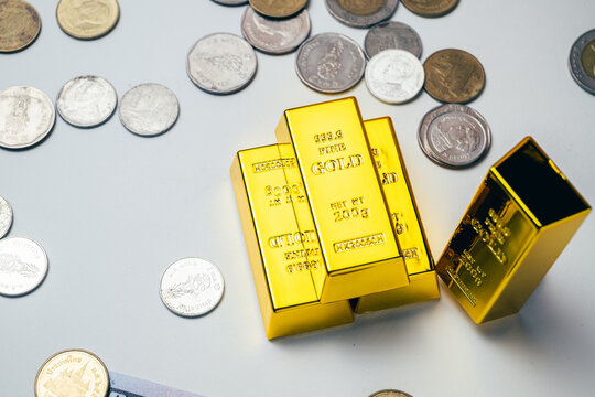 High angle view of stacked gold bars surrounded by scattered coins on a white background, representing gold investment, wealth, saving, financial security and a safe haven asset in times of inflation.