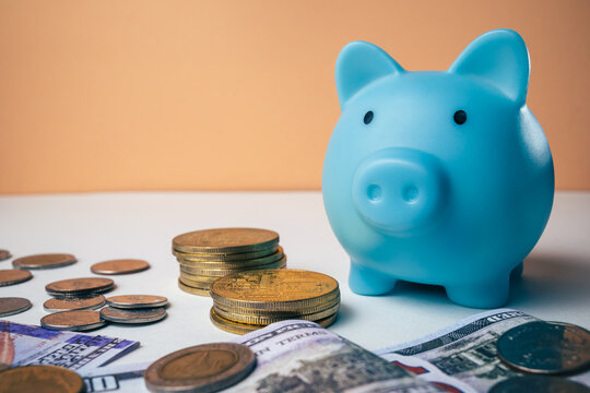 Saving money concept hand inserting a banknote into a blue piggy bank with coins. Representing the budget, personal finance, and wealth-building concept