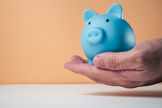 Saving money concept hand inserting a banknote into a blue piggy bank with coins. Representing the budget, personal finance, and wealth-building concept