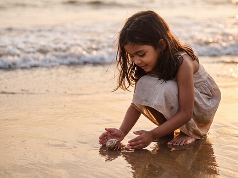 Young Indian Girl Discovers Hermit Crab on Golden Hour Beach