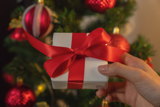 Hand holding a Christmas gift box wrapped with a red ribbon, festive celebration and seasonal shopping concept.