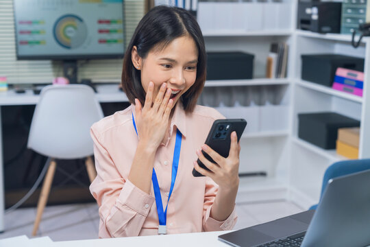 Smiling young Asian businesswoman using smartphone while working in office, mobile communication and business technology concept.