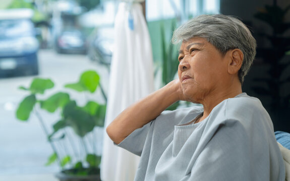 Elderly Asian woman pressing ear due to pain and inflammation while sitting at home.