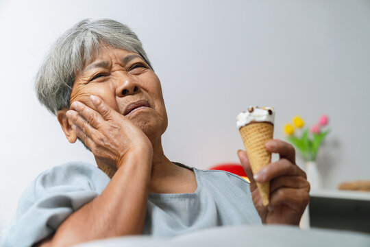 Elderly Asian woman touching her cheek after experiencing tooth sensitivity from eating ice cream, dental discomfort and oral health.