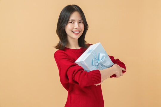 Smiling Asian woman wear a red knit sweater and holding a blue gift box.