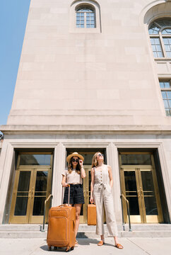 Two female travelers with orange luggage at historical building entrance