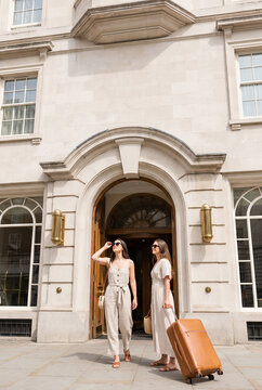Two women arriving at luxury hotel entrance with luggage