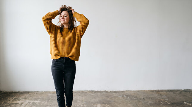 Woman in oversized mustard yellow sweater posing hands behind head