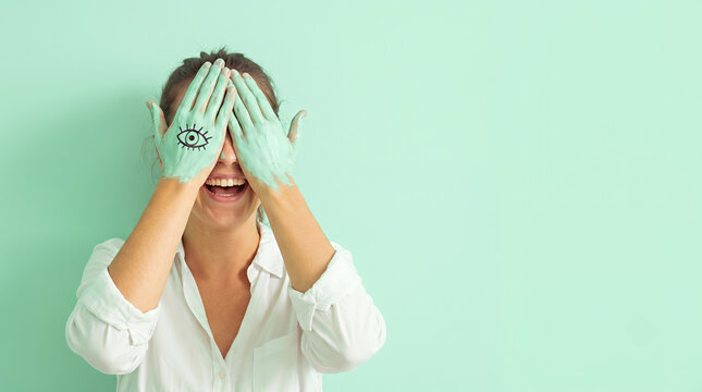Young woman with eye art painted on hands covering face turquoise