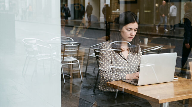 Woman working on laptop in modern office caf&eacute; through glass window