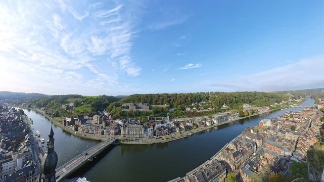 Sunny panoramic overlook of Dinant, Belgium, featuring the historic church spire, the bridge over the Meuse River, and the cliffside citadel.