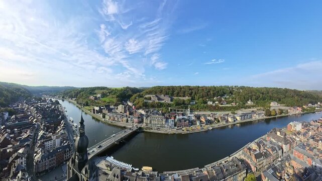 Sunny panoramic overlook of Dinant, Belgium, featuring the historic church spire, the bridge over the Meuse River, and the cliffside citadel.