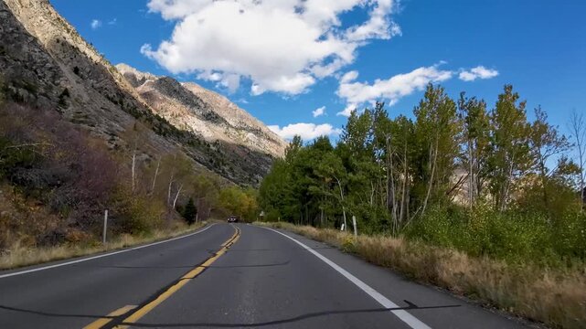 First Person View on a motorcycle ride through the Fall colors on a mountain road beside a Lake. Blue skys, puffy clouds and changing colors of Autumn tantalize the senses.