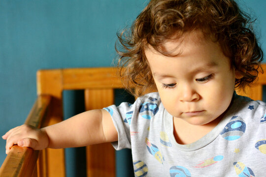 Sad toddler in the crib looking down.