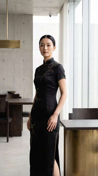 Elegant Asian woman in modern black cheongsam dress standing indoors  