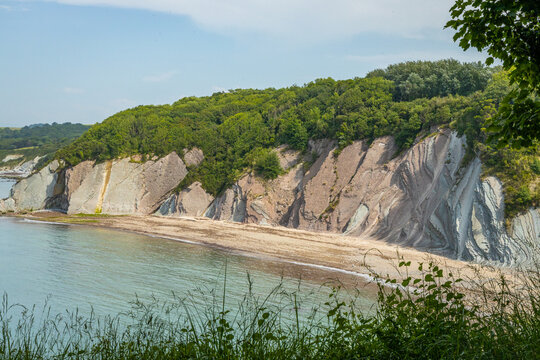 Dramatic geological flysch rock strata cliffs sloping down into a quiet cove along the Domaine d'Abbadia coastline in Hendaye, France