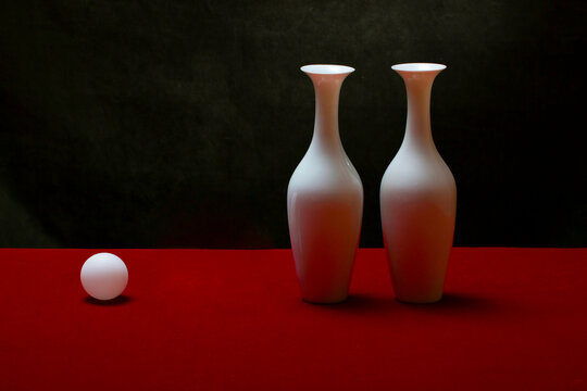 Still life with white vases and a white ball on a red table
