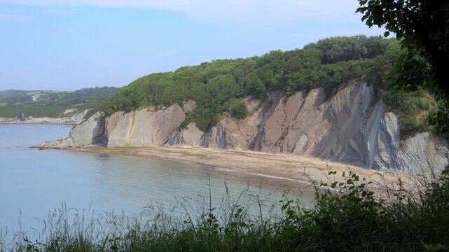 Dramatic geological flysch rock strata cliffs sloping down into a quiet cove along the Domaine d'Abbadia coastline in Hendaye, France