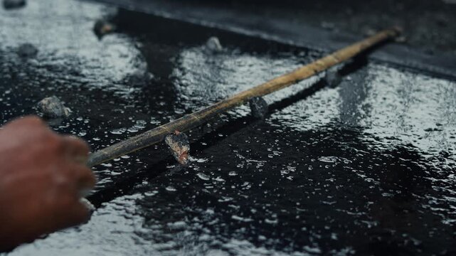 Close-up shot of anonymous hands manually scattering construction aggregate rocks onto liquid asphalt bitumen surface during road paving and civil engineering repair works.