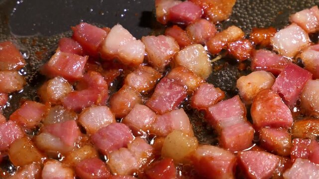 Diced bacon pieces sizzle and brown inside a hot frying pan