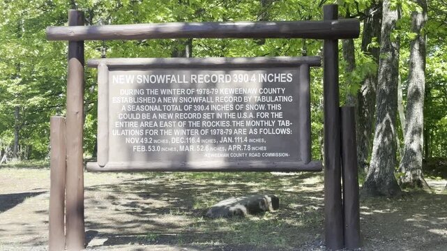 A wooden framed plaque at the Keweenaw Snow Gauge near Mohawk Michigan records 390 point 4 inches of snowfall in the 1978 to 1979 season against a leafy forest backdrop.