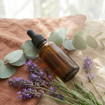 Essential oil glass dropper bottle on natural fabric with eucalyptus and lavender leaves high angle view