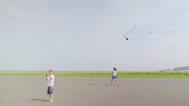 Boy and girl flying kites on a wide beach near coastal buildings slow motion children by the sea