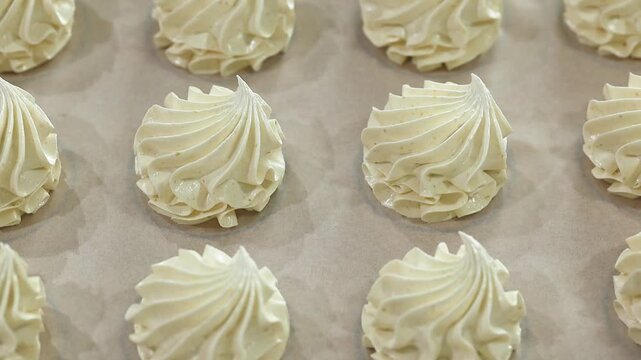 Meringue swirls displayed on parchment paper in a baking tray, highlighting their delicate shapes and glossy finishes in a bright kitchen setting