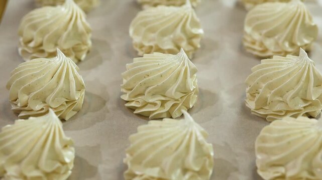 Meringue swirls displayed on parchment paper in a baking tray, highlighting their delicate shapes and glossy finishes in a bright kitchen setting